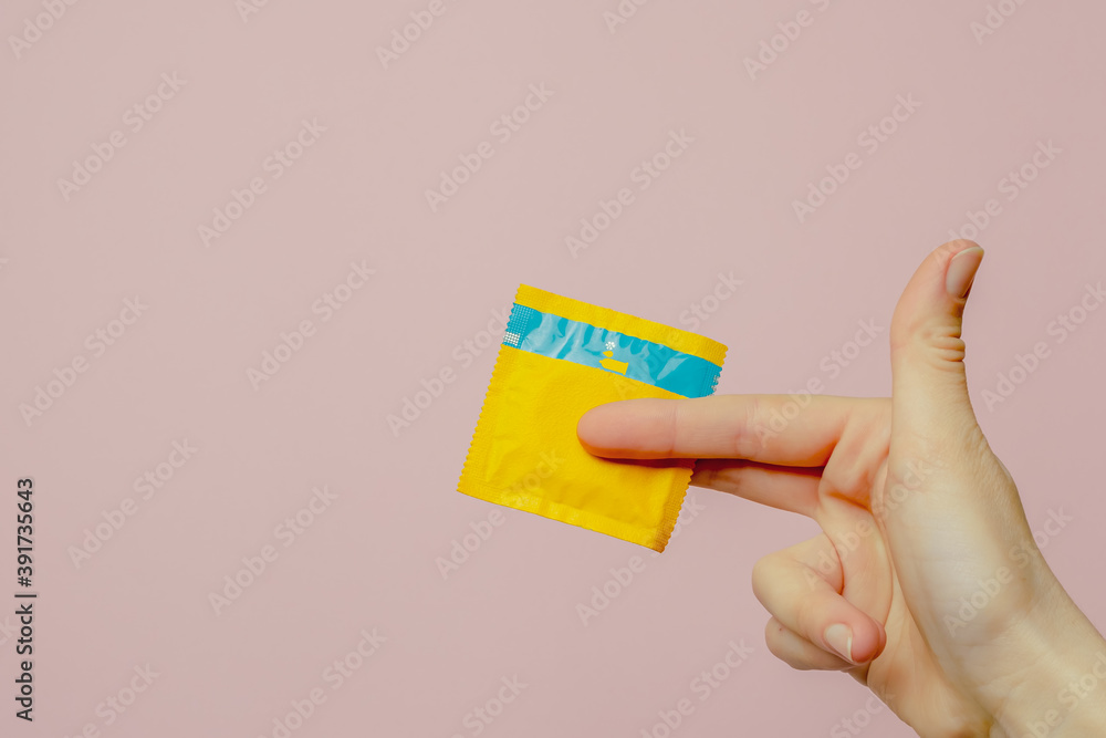 Female hand holding condom on pink background. Top view. The concept of sexual preservation Female hand holding condom on pink background. Top view. The concept of sexual preservation