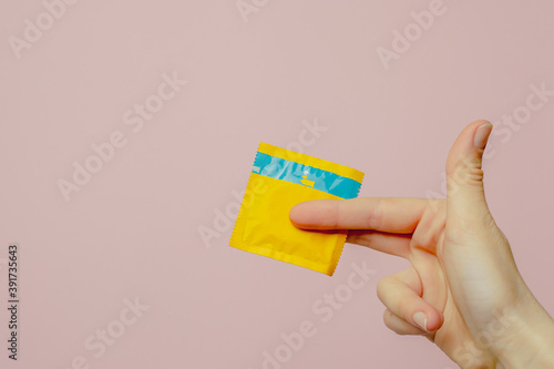 Female hand holding condom on pink background. Top view. The concept of sexual preservation