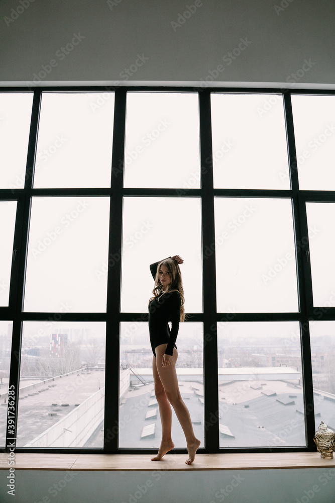 Fototapeta premium Beautiful blonde girl in a black bodysuit near a large window