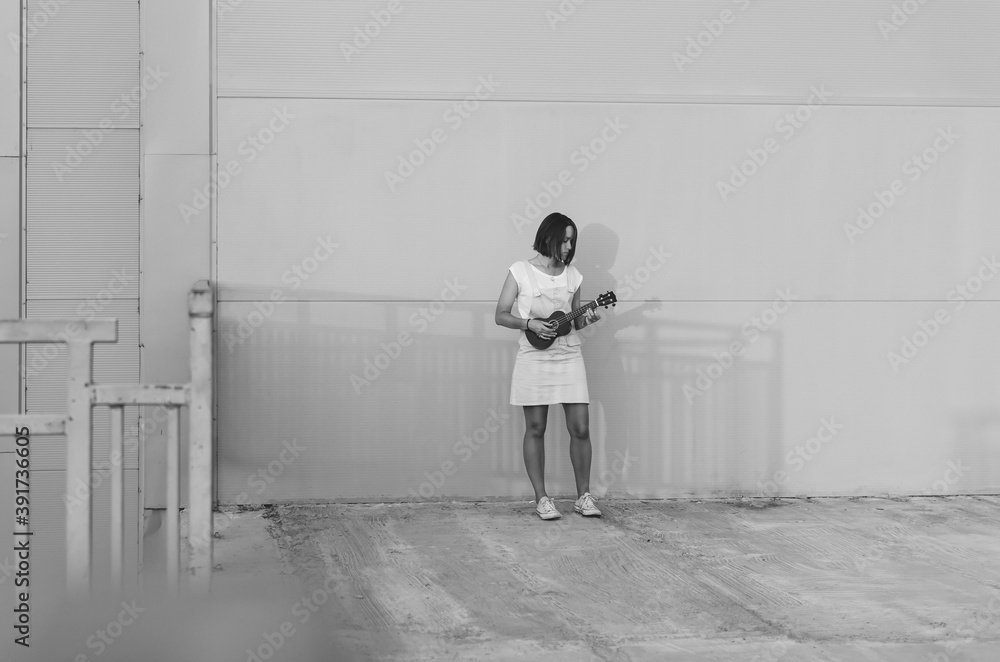 Black and white shot of Young beautiful woman playing ukulele and having fun at the background of a wall