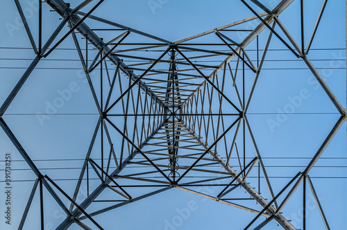 Bottom view of a Transmission tower with a blue sky. Square diagonals from the steel construction and the straight lines from the electrical cables.