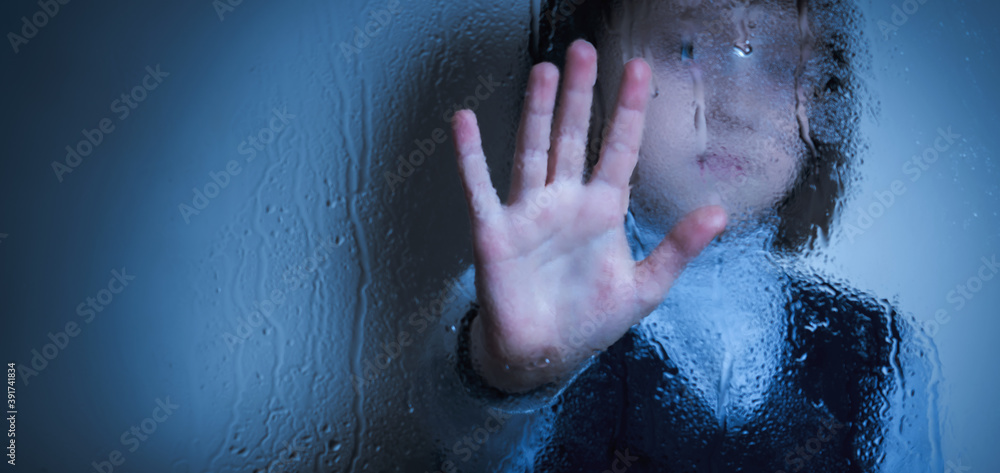 Protect children and young underage people from violence, exploitation, abuse, and neglect concept. Young girl showing stop gesture from behind wet glass. Copy space for design or text.