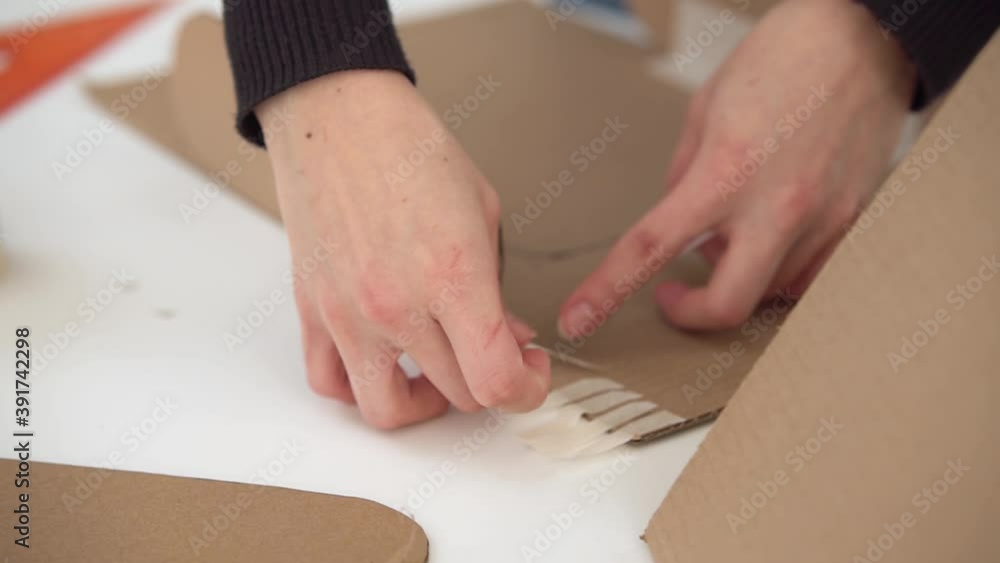 A man glues strips of masking tape to a cardboard craft. A man glues strips of masking tape to a cardboard craft.