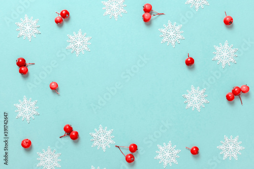 Xmas sale. Red berry, white snowflakes in shape frame on pastel blue background for greeting card. Flat lay, top view, copy space.