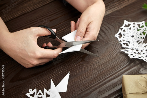 Hands cutting white paper snowflakes over wooden table