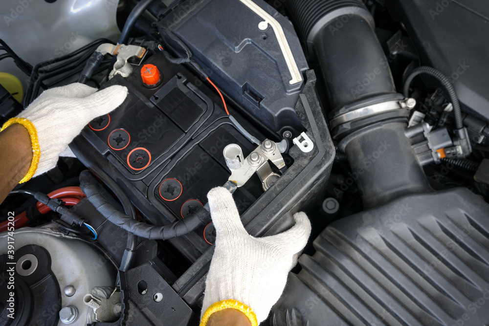 The auto mechanic is replacing the car battery in engine compartment. The auto mechanic is replacing the car battery in engine compartment.