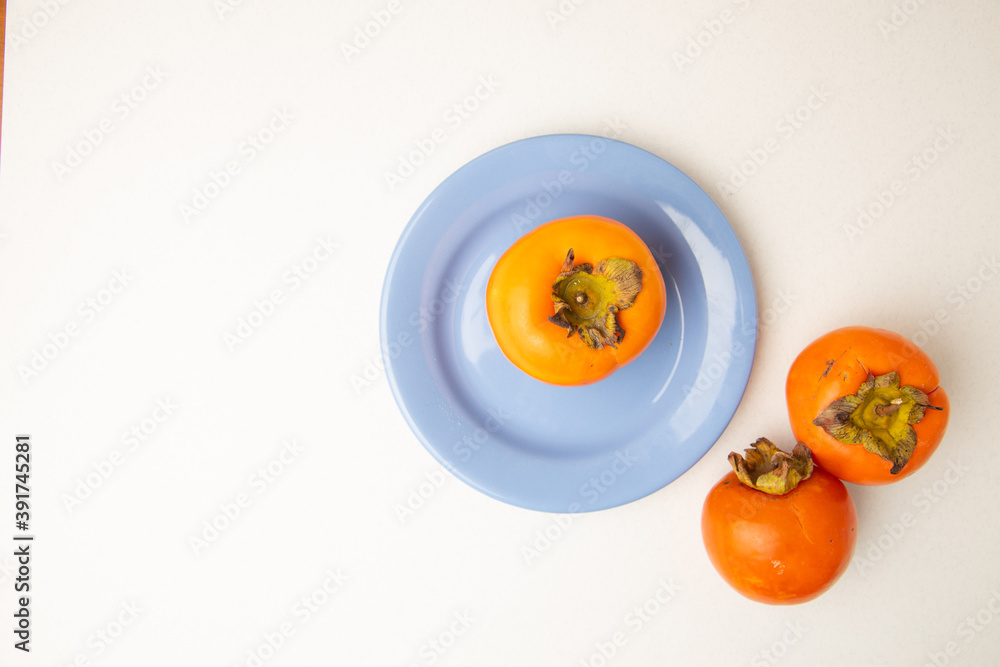 Persimmon fruit on white background and blue plate Persimmon fruit on white background and blue plate