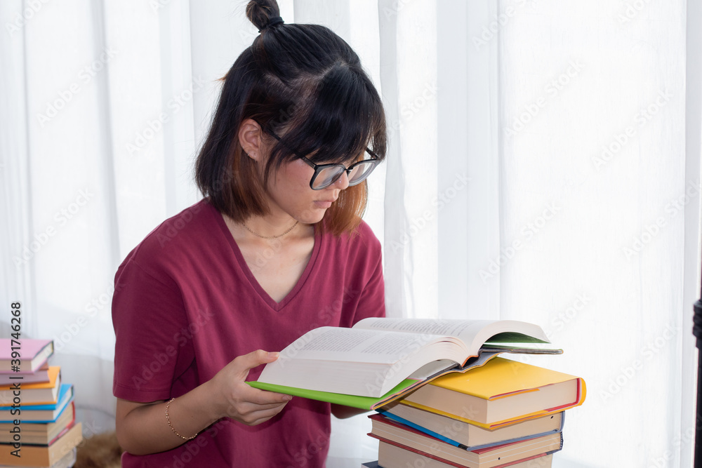 Serious Asian teen girl with eyeglasses pay attention reading book for examination or competition, university student read book at home get headache, woman casual with stack of books learning at home Serious Asian teen girl with eyeglasses pay attention reading book for examination or competition, university student read book at home get headache, woman casual with stack of books learning at home