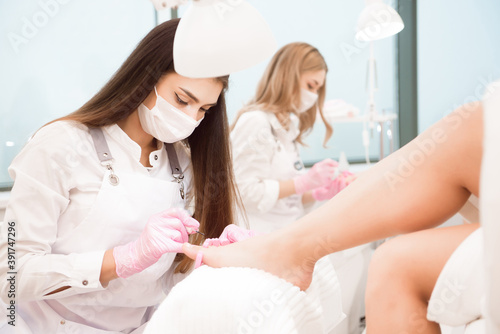 Foot treatment for two friends or sisters in SPA salon. Nail artist in beauty salon making pedicure for clients feet.
