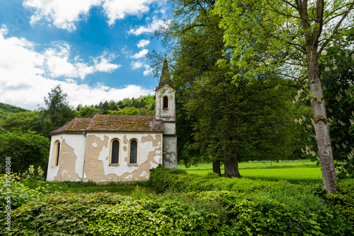 Small withered chapel in Bavaria standing amidst trees in summer with blue sky and clouds