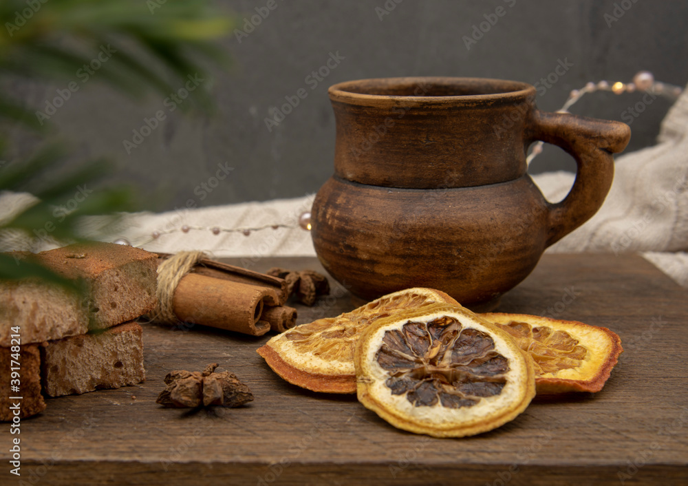 A brown ceramic mug, sweets and aromatic spices stand on a wooden tray against a gray wall.