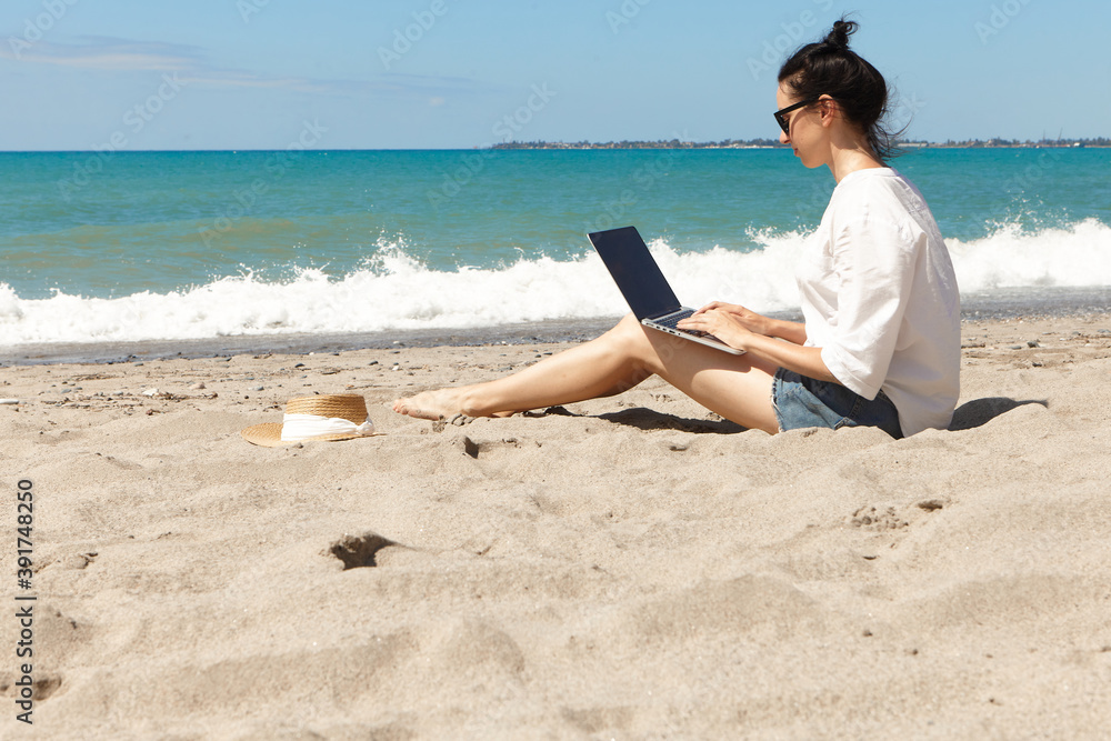 Young woman using laptop computer on a beach. Vacation lifestyle communication. Freelance work concept