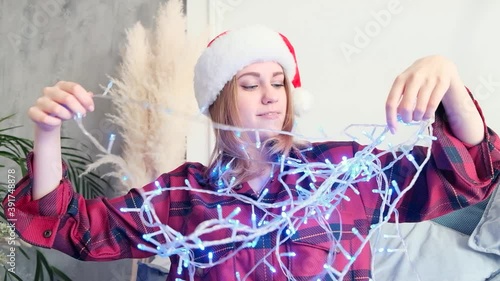 Christmas, home decor and holidays concept. Portrait of a young attractive woman untangling a garland for decoration. Slow motion