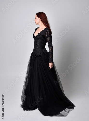 full length portrait of woman wearing black gothic dress, Standing pose against a studio background.