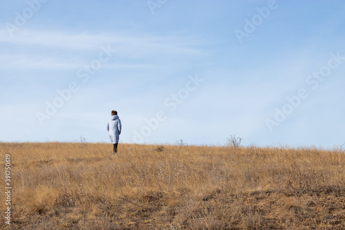 Woman in a jacket walking on the steppe in autumn.