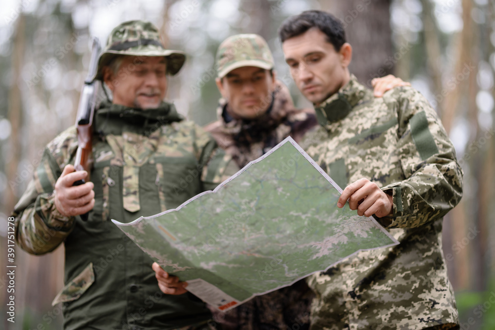 Topographical Map in Hands of Hunters in Forest.