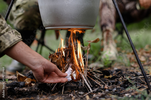 Hand of Man Sets Fire under Cooking Pot in Forest.