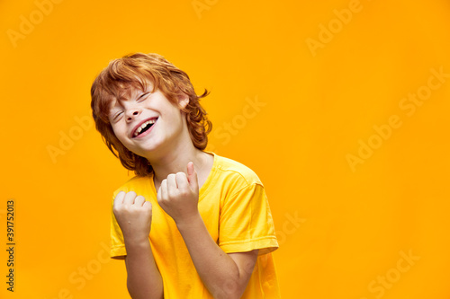 Expressive red-haired boy gestures with his hands yellow isolated background holds his hands in fists © SHOTPRIME STUDIO