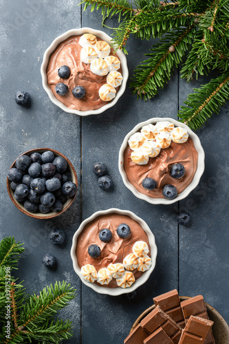 Chocolate mousse with meringues and blueberries on top. Chocolate dessert on the blue wood with Christmas decoration. Flat lay