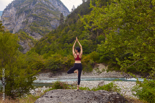 Yoga classes in nature. The concept of playing sports alone. Social exclusion. A woman does yoga on rocks, near a mountain river flows
