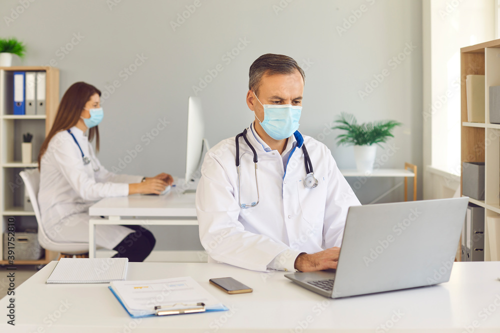 Man and woman hospital workers in protective masks working in office keeping distance. Man and woman hospital workers in protective masks working in office keeping distance.