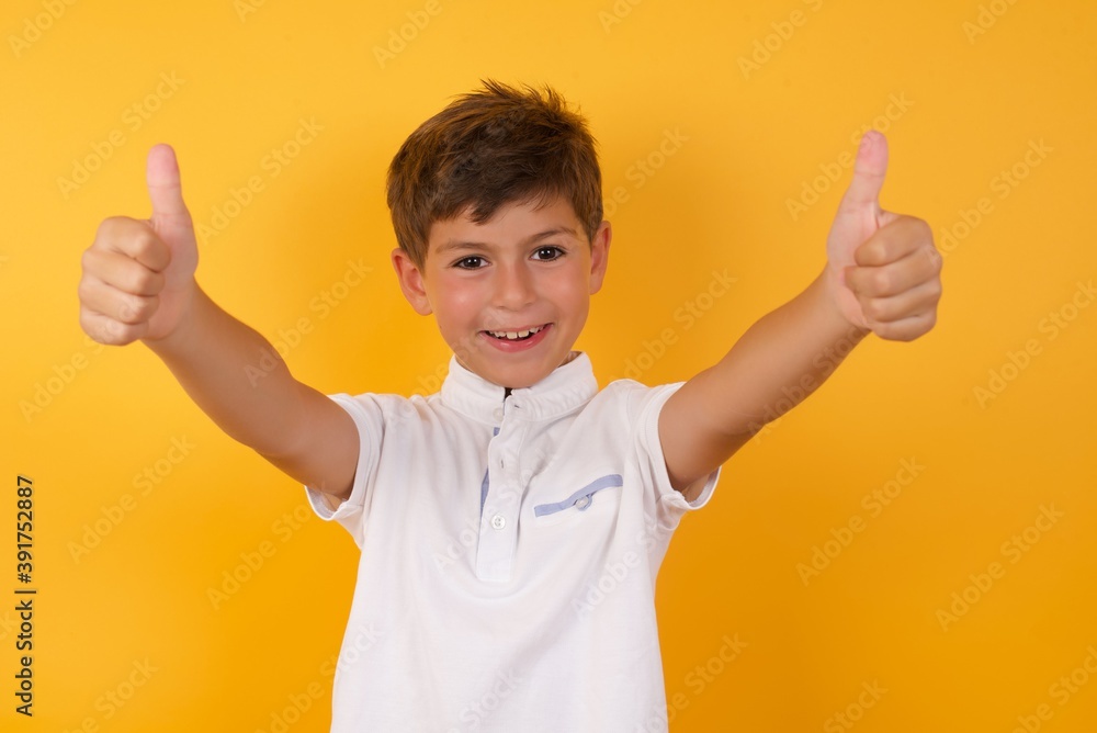Amazed Cute Caucasian little boy standing against yellow background points down with fore fingers, opens mouth being shocked. Advertisement concept. Amazed Cute Caucasian little boy standing against yellow background points down with fore fingers, opens mouth being shocked. Advertisement concept.
