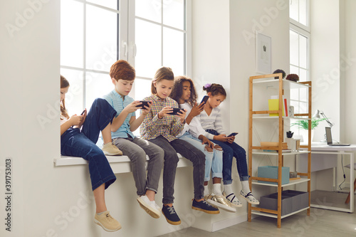 Kids sitting on windowsill, playing games on mobile phones and ignoring each other photo