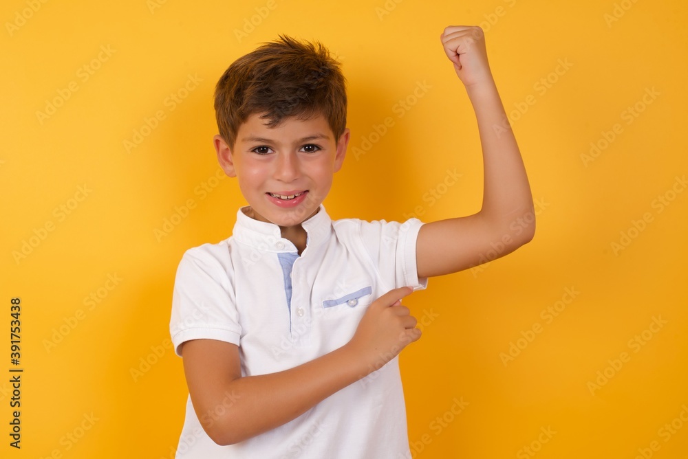 Smiling Cute Caucasian little boy standing against yellow background raises hand to show muscles, feels confident in victory, strong and independent. Smiling Cute Caucasian little boy standing against yellow background raises hand to show muscles, feels confident in victory, strong and independent.