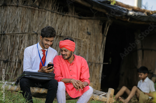 Young indian agronomist or banker showing some information to farmer in smart phone