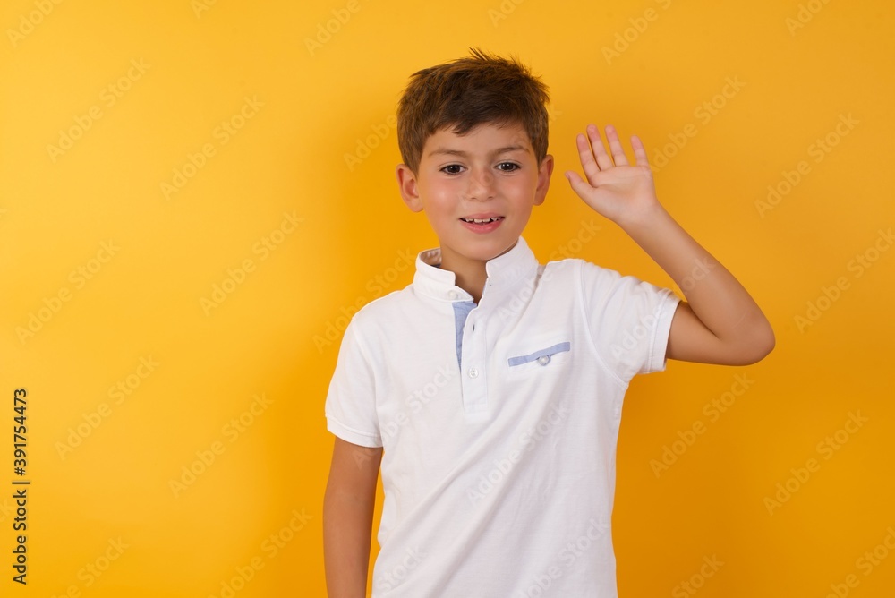 Young handsome Caucasian little boy standing against yellow wall waiving saying hello or goodbye happy and smiling, friendly welcome gesture. Young handsome Caucasian little boy standing against yellow wall waiving saying hello or goodbye happy and smiling, friendly welcome gesture.