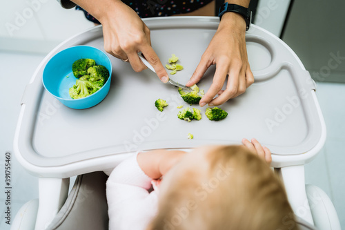 baby eating broccoli with hands in early stages of baby-led weaning at home