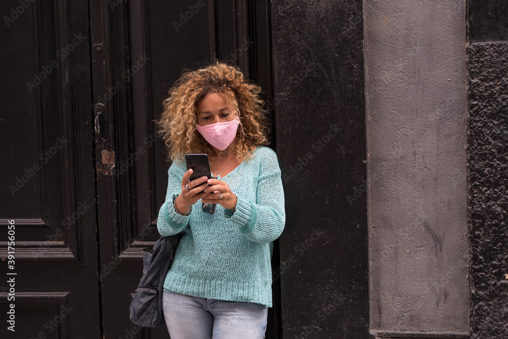 Fototapeta premium Adult woman wear protection mask against covid-19 coronavirus virus emergency - protect yourself people with anti virus accessory - female in the town with phone reading news about health