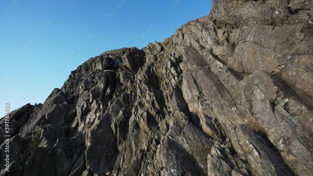 A man climbing a steep rocky mountainside cliff A man climbing a steep rocky mountainside cliff