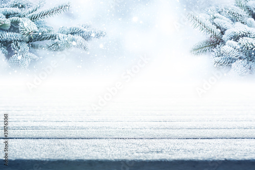 Empty frosty wooden boards with fir branches and snowfall. Atmospähric winter background with short depth of field for christmas and advent concepts. Space for design and text.