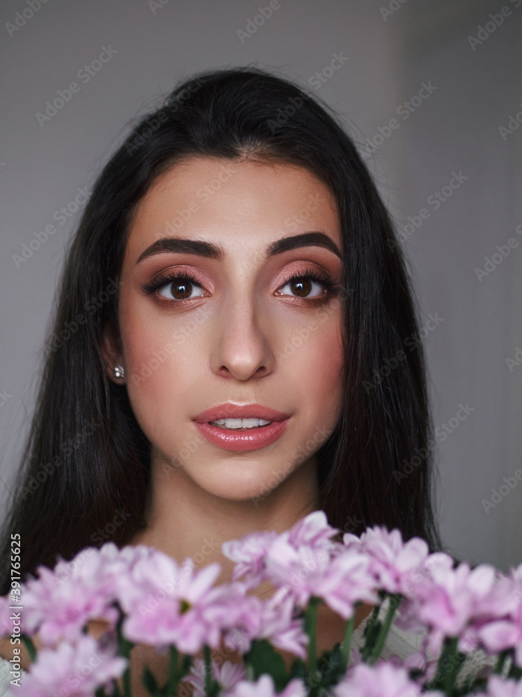 Magnificent portrait of a beautiful brunette young woman with perfect skin makeup closeup flowers bouquet