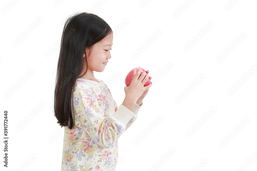 Smiling asian little girl holding red apple in hands and looking it over white background. Side view Smiling asian little girl holding red apple in hands and looking it over white background. Side view