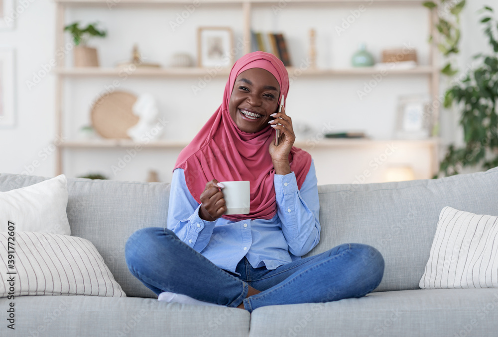 Cheerful Black Muslim Lady Talking On Cellphone And Drinking Coffee At Home Cheerful Black Muslim Lady Talking On Cellphone And Drinking Coffee At Home