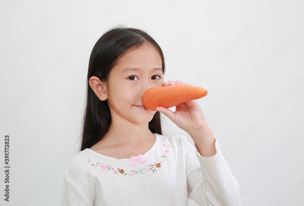 Funny face asian little girl making long nose with carrot on white background Funny face asian little girl making long nose with carrot on white background