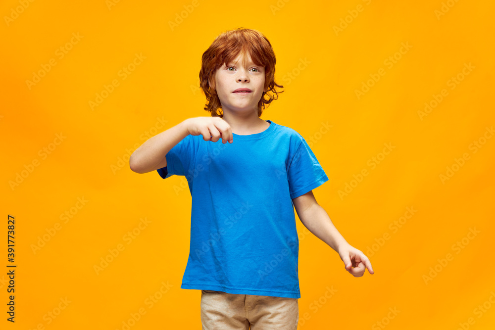 Red-haired child in a blue t-shirt gestures with his hands emotions yellow isolated background Red-haired child in a blue t-shirt gestures with his hands emotions yellow isolated background