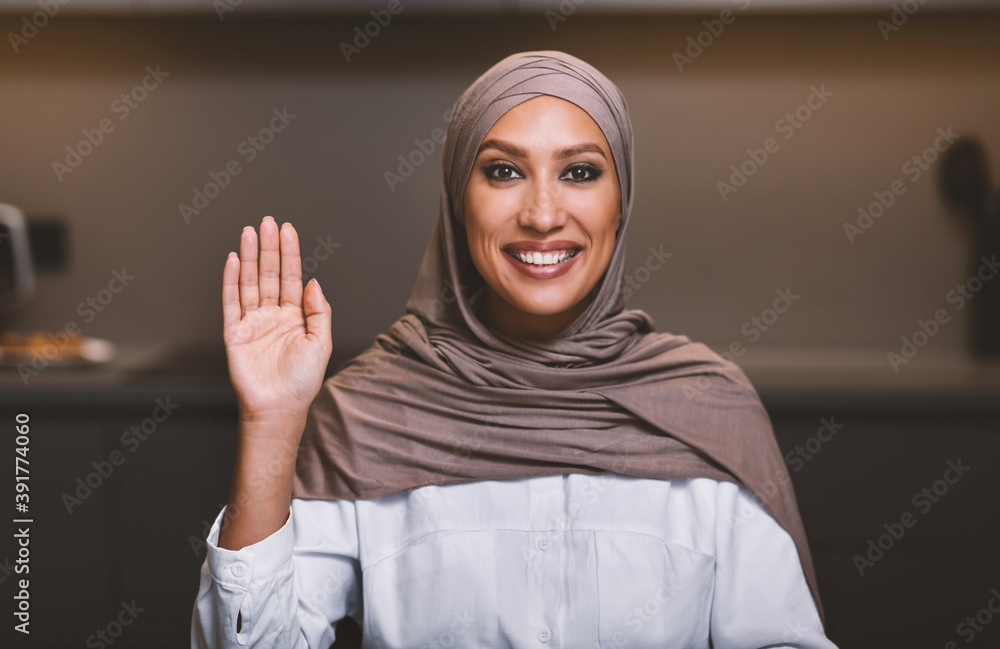 Muslim Lady In Hijab Waving Hand Sitting In Kitchen Muslim Lady In Hijab Waving Hand Sitting In Kitchen