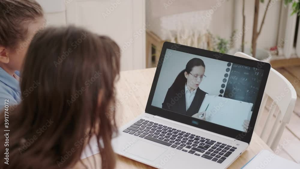 Over the shoulder shot. Children learn remotely by videoconference with the teacher online on a laptop Over the shoulder shot. Children learn remotely by videoconference with the teacher online on a laptop