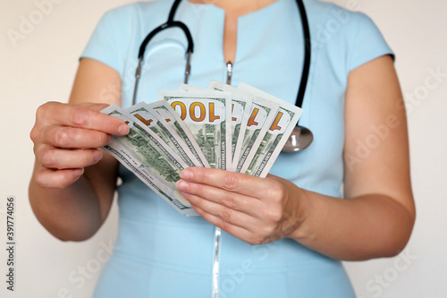 Woman doctor with US dollars in hands. Concept of medical staff salary, money for medical exam or expensive health care