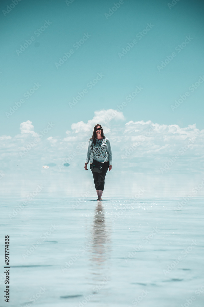 young woman walking in the salt flats over the mirrored water, celestial sky, heat mountains and clouds young woman walking in the salt flats over the mirrored water, celestial sky, heat mountains and clouds