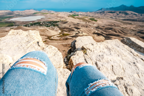 Knees of a woman in torn blue jeans against the background of a mountainous hilly landscape