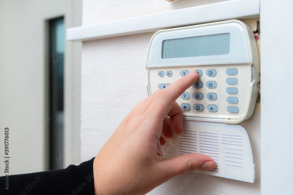 Hand entering alarm system password of an apartment, home or business office. Surveillance and protection console against rubbery and thief Hand entering alarm system password of an apartment, home or business office. Surveillance and protection console against rubbery and thief