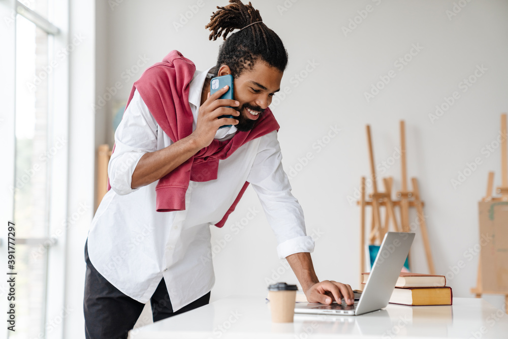 Happy african american guy talking on cellphone and working with laptop Happy african american guy talking on cellphone and working with laptop