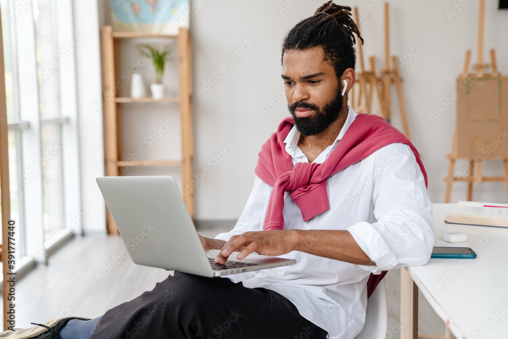 Serious african american guy in earphones working with laptop Serious african american guy in earphones working with laptop