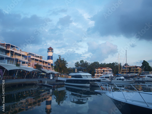 Luxurious yacht club, expensive yachts, buildings with luxury apartments, lighthouse in the evening at sunset. Reflection on the surface of water. Nice view of coastal town. Phuket, Boat Lagoon, Thai