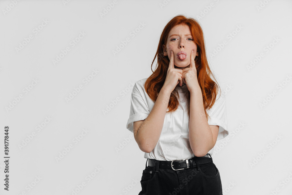 Ginger girl showing her tongue and pointing fingers at her cheeks Ginger girl showing her tongue and pointing fingers at her cheeks