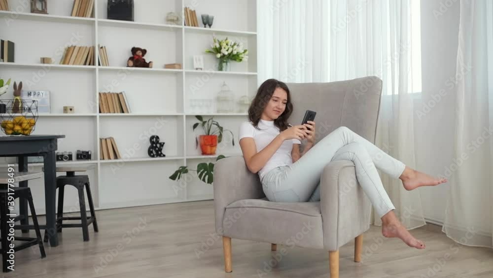 Pretty young girl sitting in the chair indoors and using smartphone. Pretty young girl sitting in the chair indoors and using smartphone.